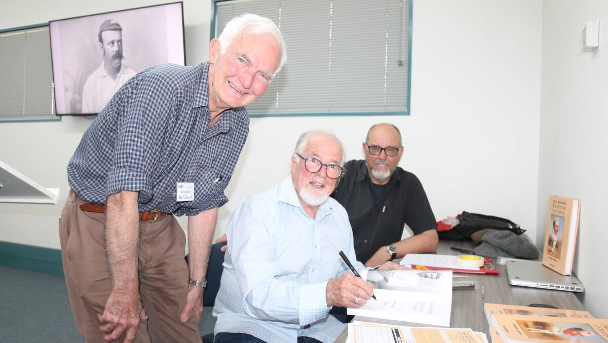 With Billy Murdoch looking on from the big screen, authors Richard Cashman and Ric Sissons (rear) sign a book for U3A member Graham McClintock.