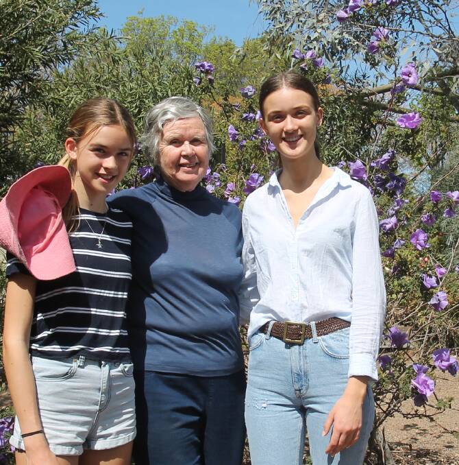Win Main with visiting granddaughters Freya and Indie in front of a purple-flowered Alogyne plant, a WA variety that blooms beautifully with little or no water. 