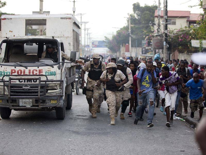 Gunfire forces people to take cover behind a truck during a protest against Haiti's president.